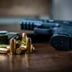 Close view of a handgun with bullets on a wooden surface, emphasizing firearms and ammunition.