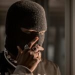 A person wearing a black balaclava adorned with rings and necklaces, creating an air of mystery.