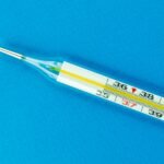 Close-up shot of a traditional glass thermometer on a vibrant blue background.